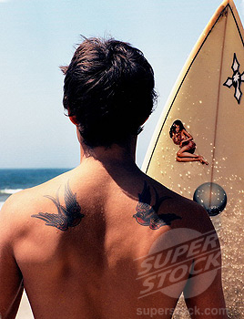 Tattooed surfer at beach, rear view.